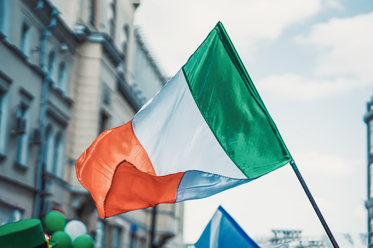 Flag of Ireland close up on background of blue sky, city street. Saint Patrick day holiday