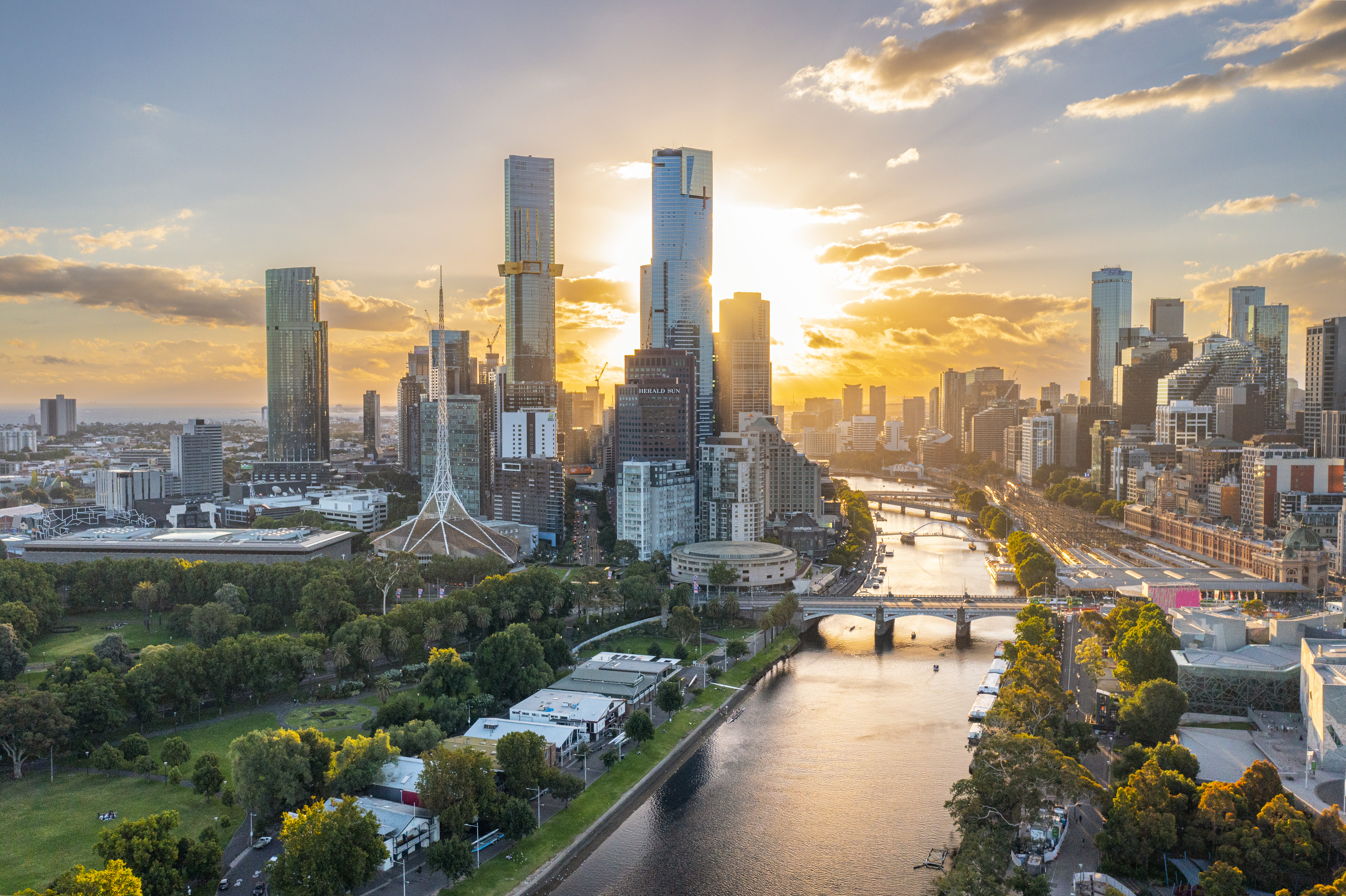 Sun sets over the Yarra River in the distance. Melbourne skyscrapers silhouetted by the sun. 