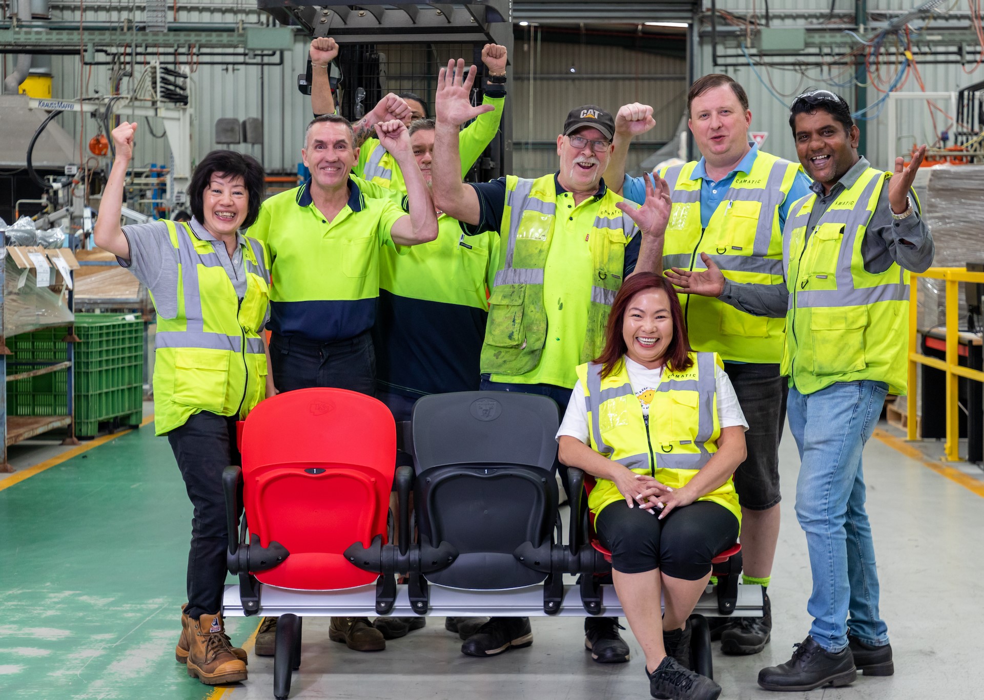The Cematic Seating team stand in high vis gear around their products smiling with hands in the air cheering. One woman is seated at the front on one of Cematic's showcase seats.