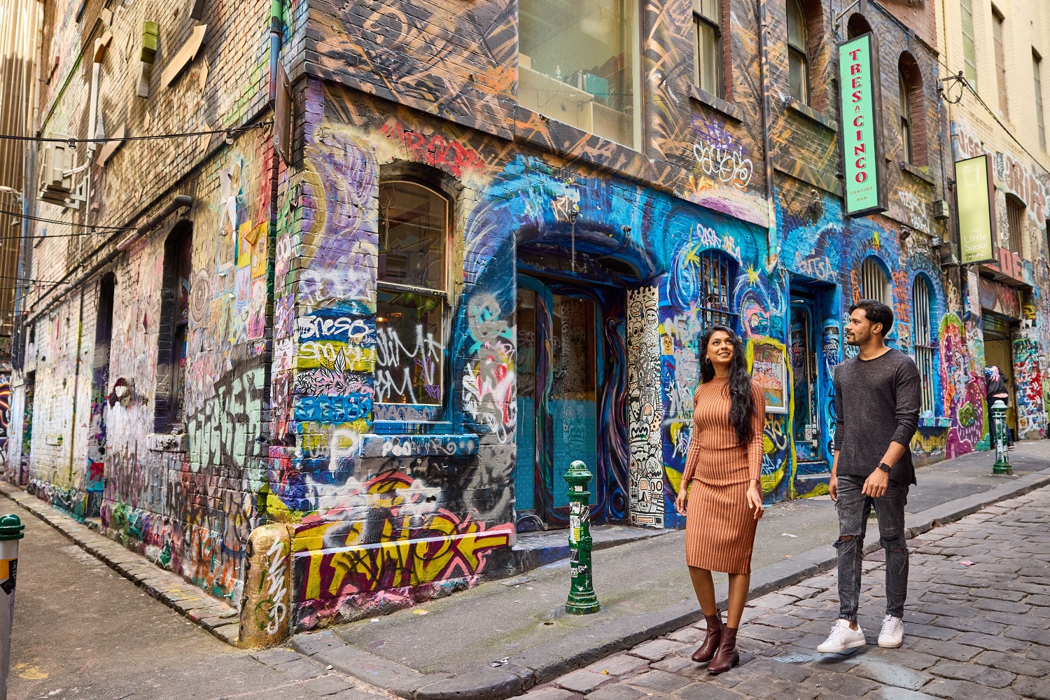 A young man and woman walking down Hosier Lane in Melbourne's city. The walls of the laneway are full of street art